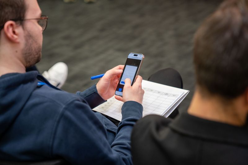 Lauri Alho, a jury member at the Orange Camara API Hackathon in Warsaw, Poland, uses a smartphone to evaluate a live application, demonstrating engagement with Network as Code and Camara APIs.