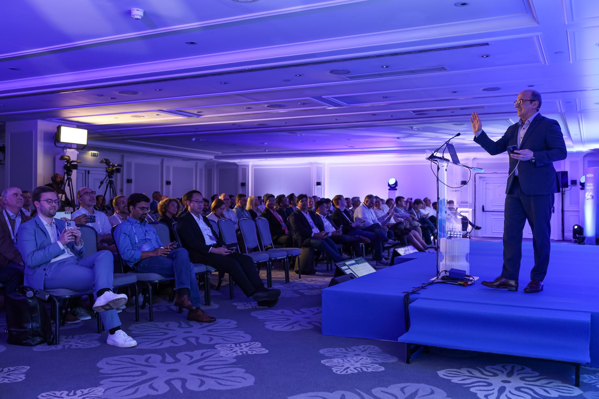 Lauri Alho capturing a picture of Shkumbin Hamiti, who is presenting a Network as Code keynote for enhanced fraud detection to customers at the Nokia Core User Group 2025 in Lisbon, Portugal, demonstrating multi-operator API value.